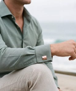 Close-up of a person wearing a sage-green shirt with rolled sleeves, extending an arm outdoors.