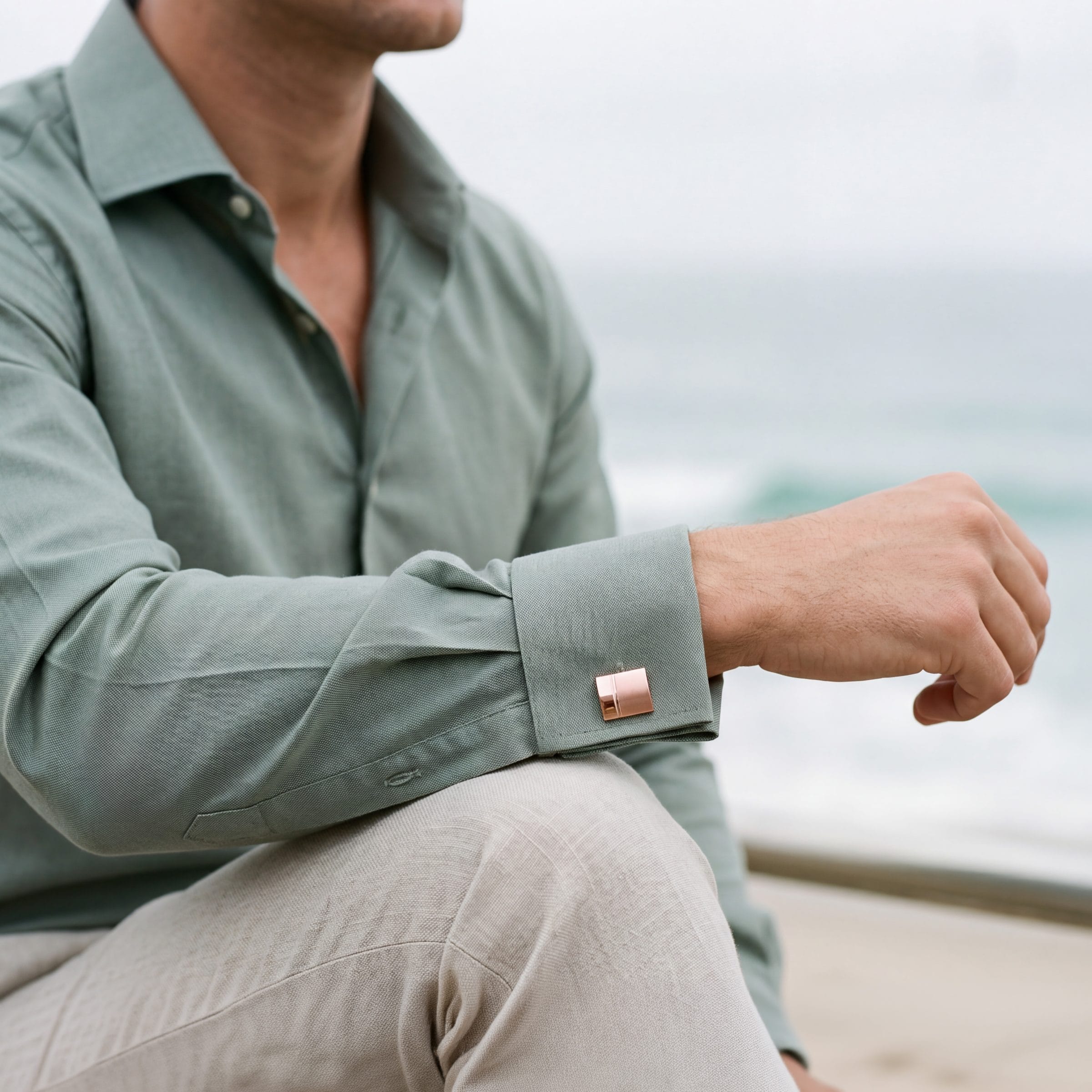 240-10M | Cudworth Close-up of a person wearing a sage-green shirt with rolled sleeves, extending an arm outdoors.
