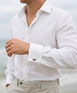 Person wearing a white linen shirt with rolled sleeves, arms crossed, near a beach. (informative)