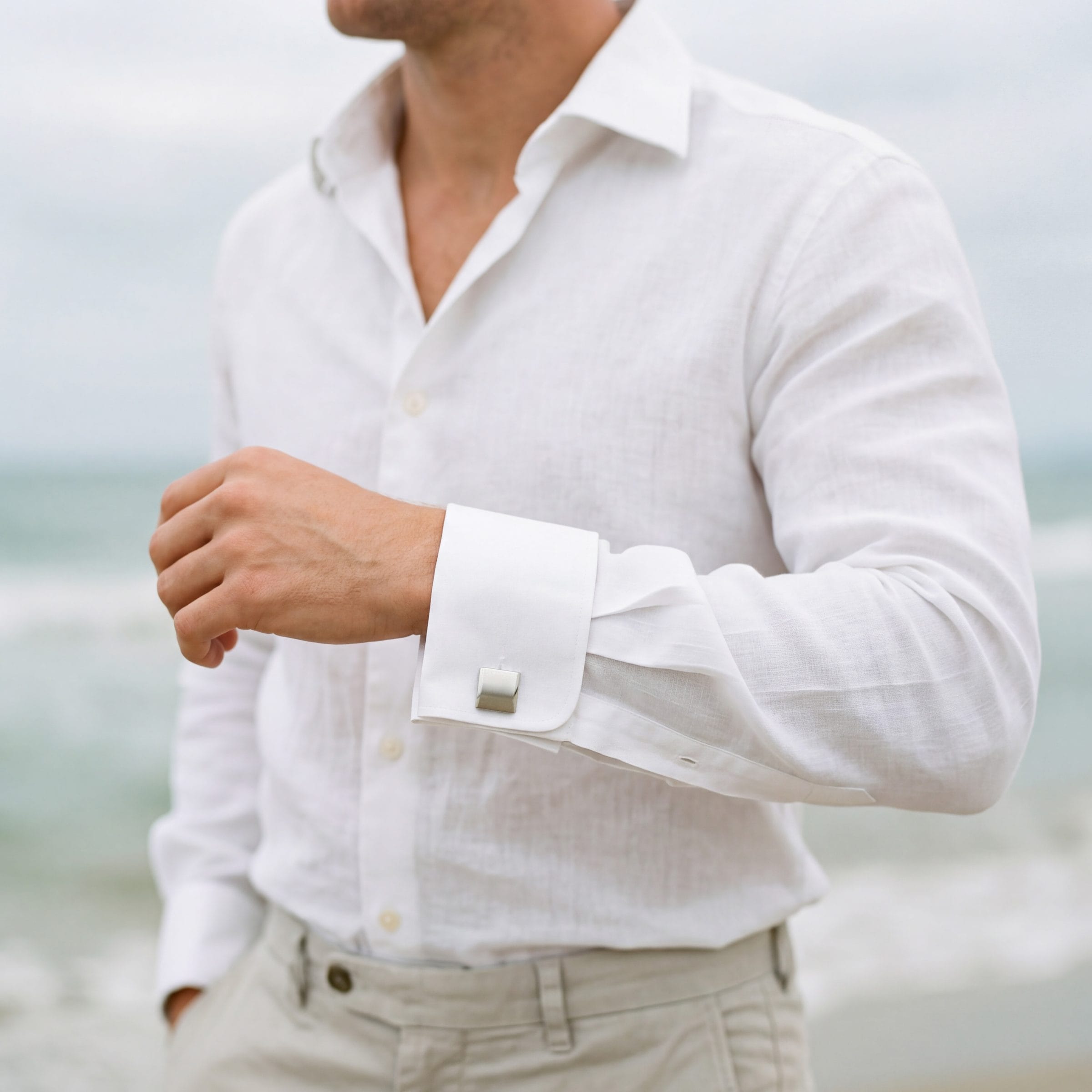 241-45M | Cudworth Person wearing a white linen shirt with rolled sleeves, arms crossed, near a beach. (informative)