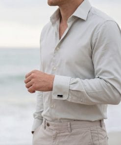 Man wearing a light beige button-down shirt standing at the beach, torso visible from chest to hips