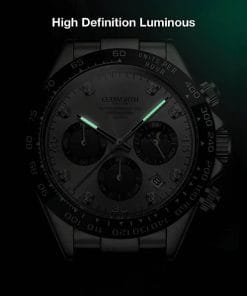 Close-up of a stainless steel chronograph watch in dim light, with glowing green hour and minute hands.