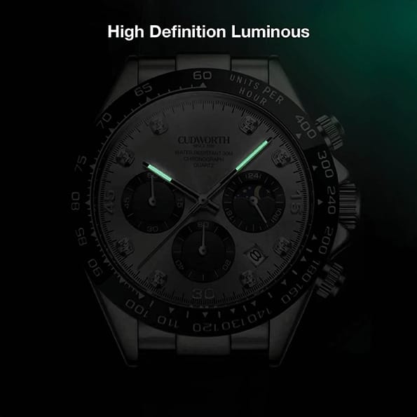 CU2875WTSV05 | Cudworth Close-up of a stainless steel chronograph watch in dim light, with glowing green hour and minute hands.